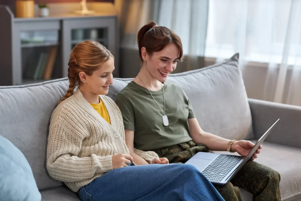 Woman in army uniform sitting with daughter on a lounge - they are using a laptop to make a DVA referral with Ryre Care